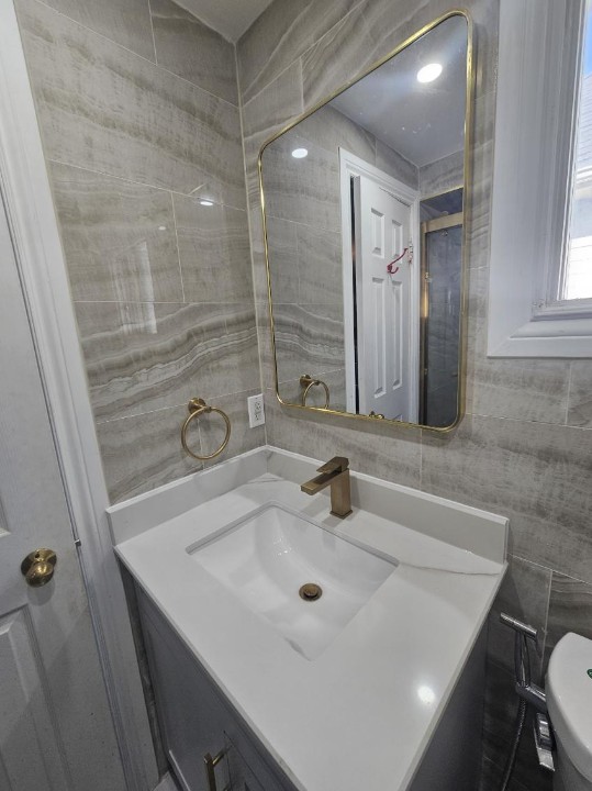 Finished washroom vanity with gold fixtures and full-height grey tile