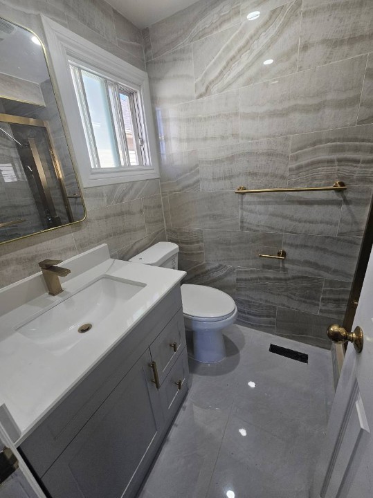 Completed grey tiled washroom with vanity, toilet and gold fixtures