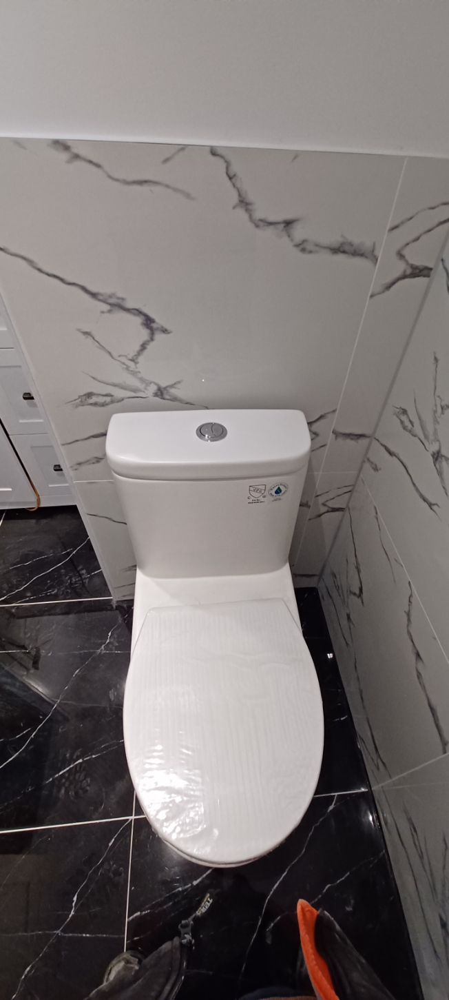 New toilet installed against marble-look wall tile and black floor tile