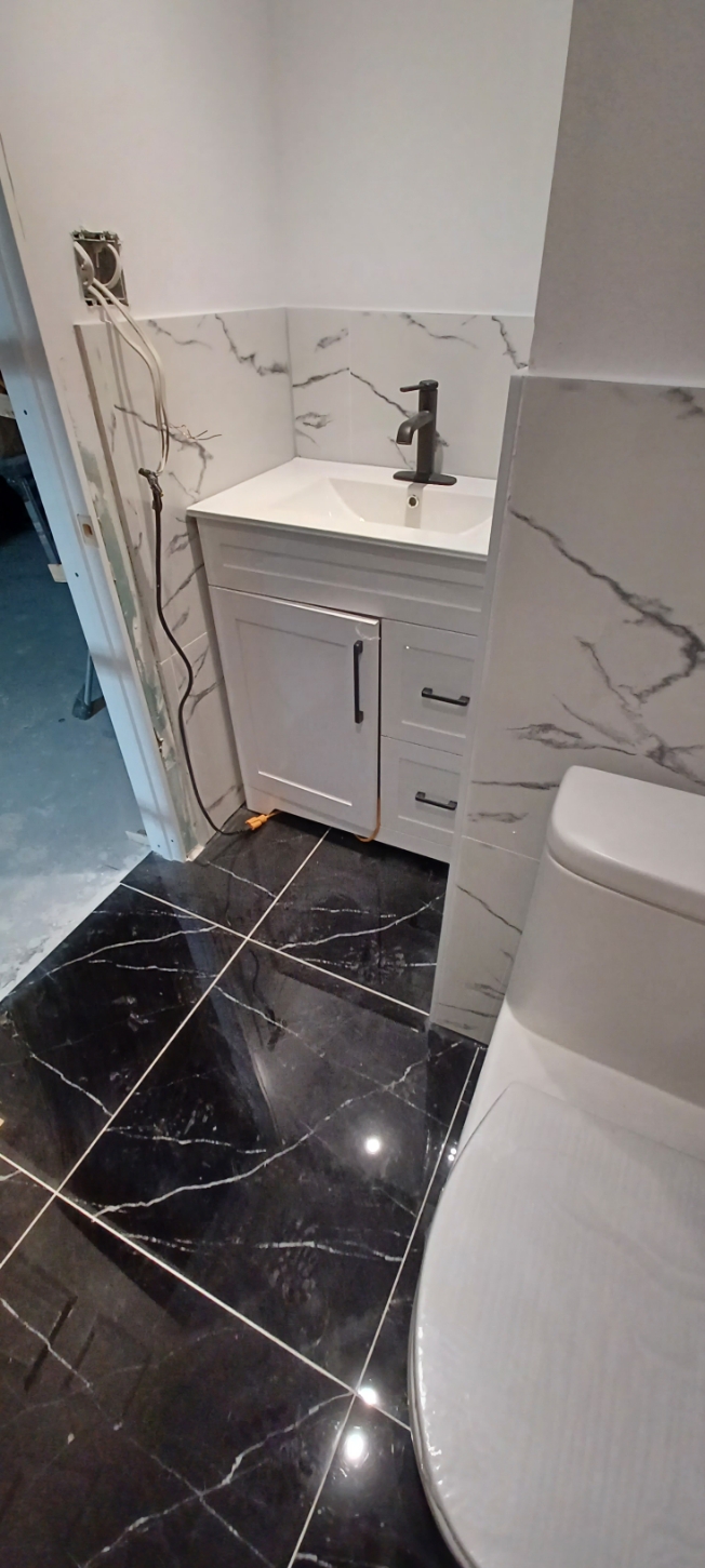 Compact white vanity with dark faucet and marble-look tile surround