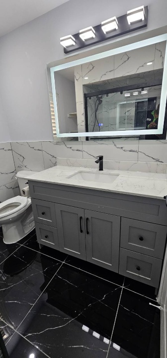 Large grey washroom vanity with illuminated mirror and black fixtures